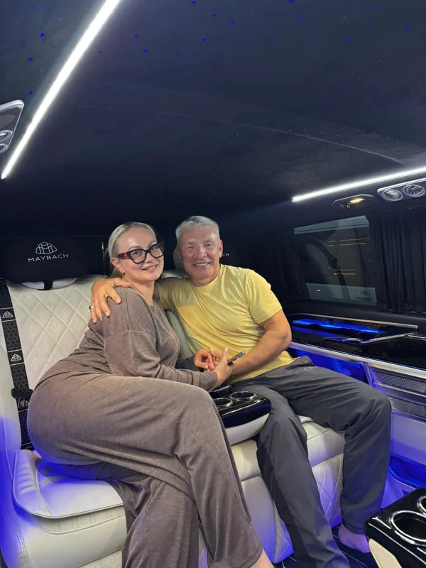 Mavi aydınlatmalı minibüs kabinindeki açık renk koltukta oturan iki yolcu.